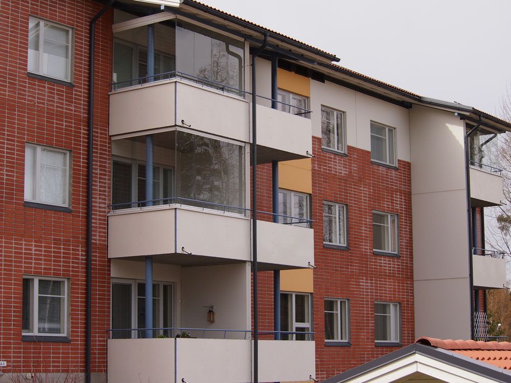 Tiilikerrostalo, jossa on parvekkeita, ikkunoita sekä valkoisia ja oransseja yksityiskohtia.