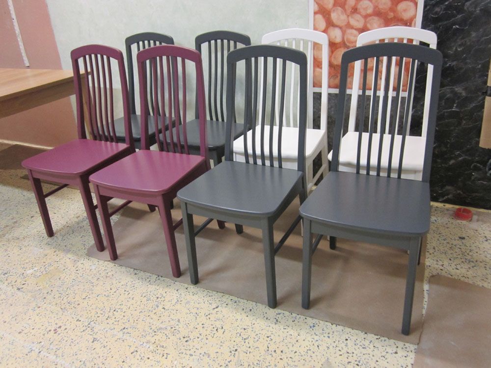 Seitsemän eri väreillä (violetti, harmaa ja valkoinen) maalattua puista tuolia aseteltuna kuviolliselle lattialle.