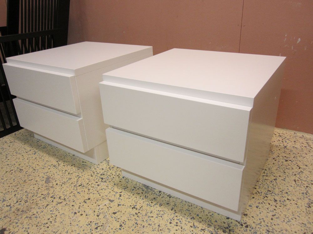 Kaksi valkoista, modernia yöpöytää, joissa kummassakin on kaksi laatikkoa, kuviollisella lattialla.