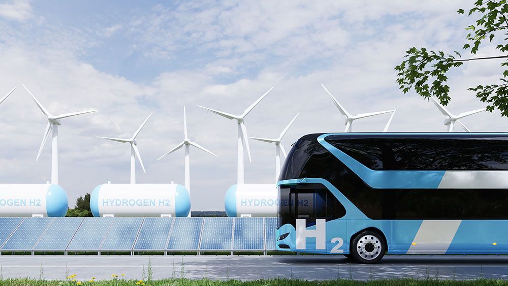 Wasserstoffbetriebener Doppeldeckerbus mit Windkraftanlagen und Solarpaneelen, blau-weißes Design, sonnige Außenkulisse.