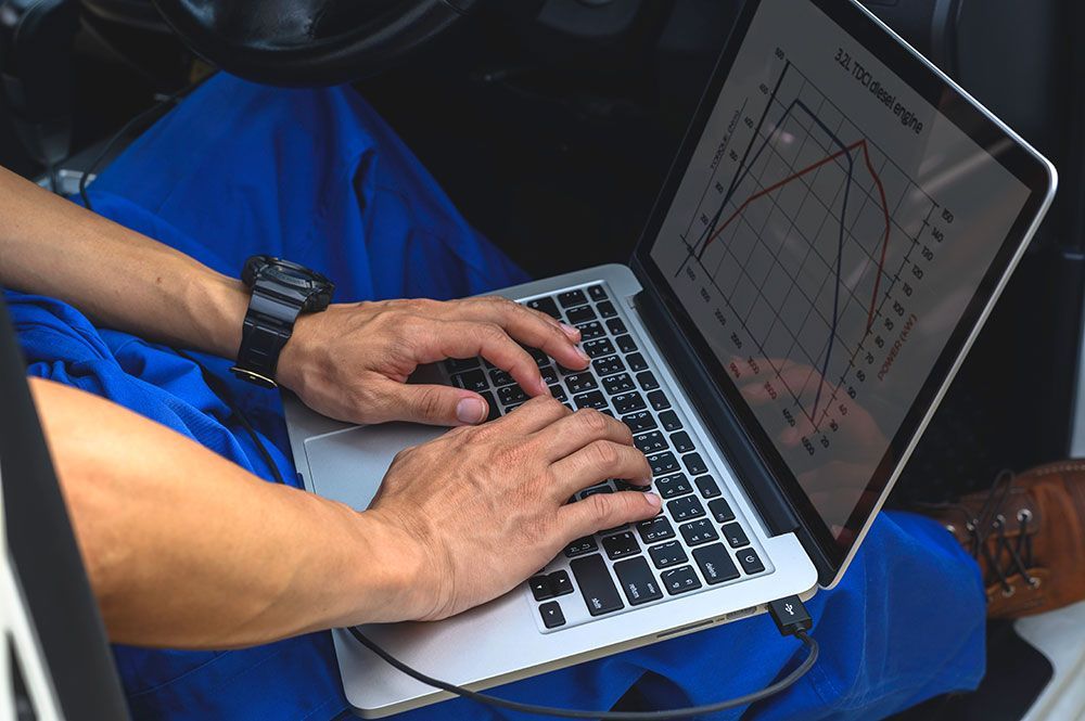 Eine Person in blauem Overall sitzt in einem Auto und betrachtet einen Laptop.