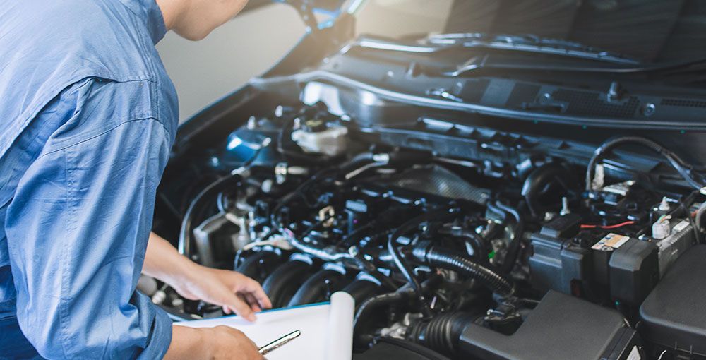 Ein Mechaniker untersucht in einer Autowerkstatt mit einem Klemmbrett einen Automotor.