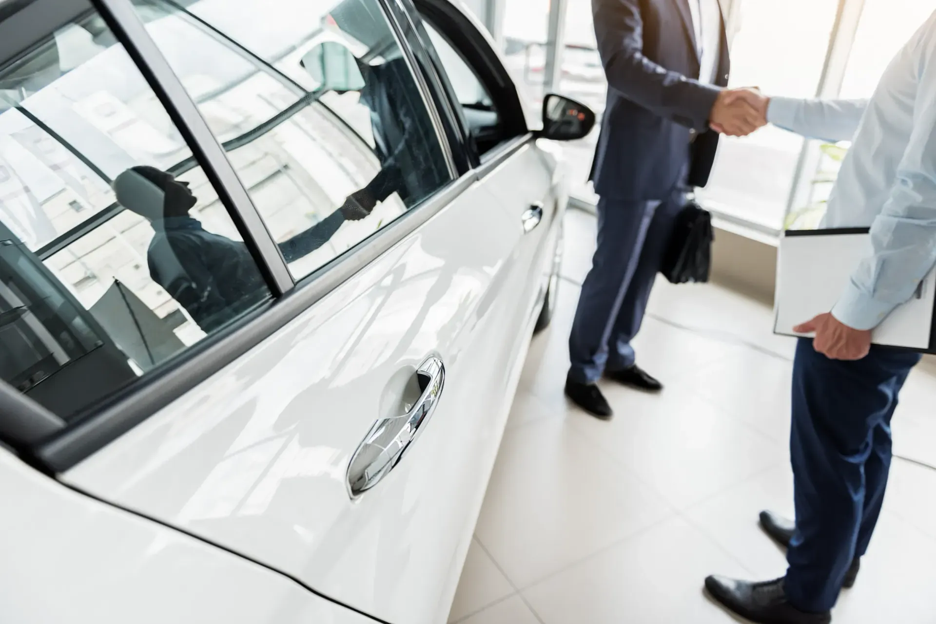 Dos hombres se dan la mano delante de un coche en una sala de exposición.