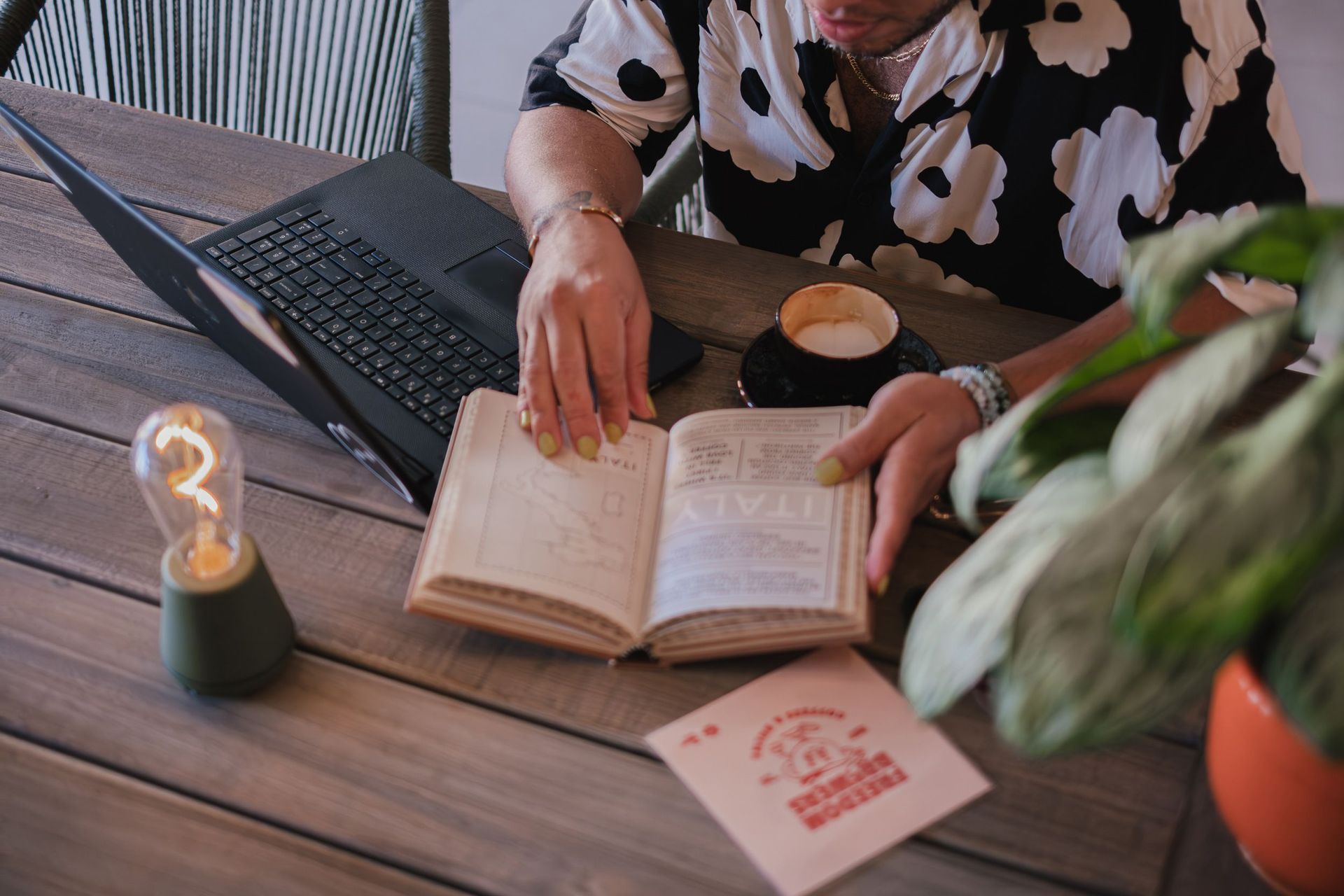Person writing in an open notebook beside a laptop and glowing number lamp on a wooden table.