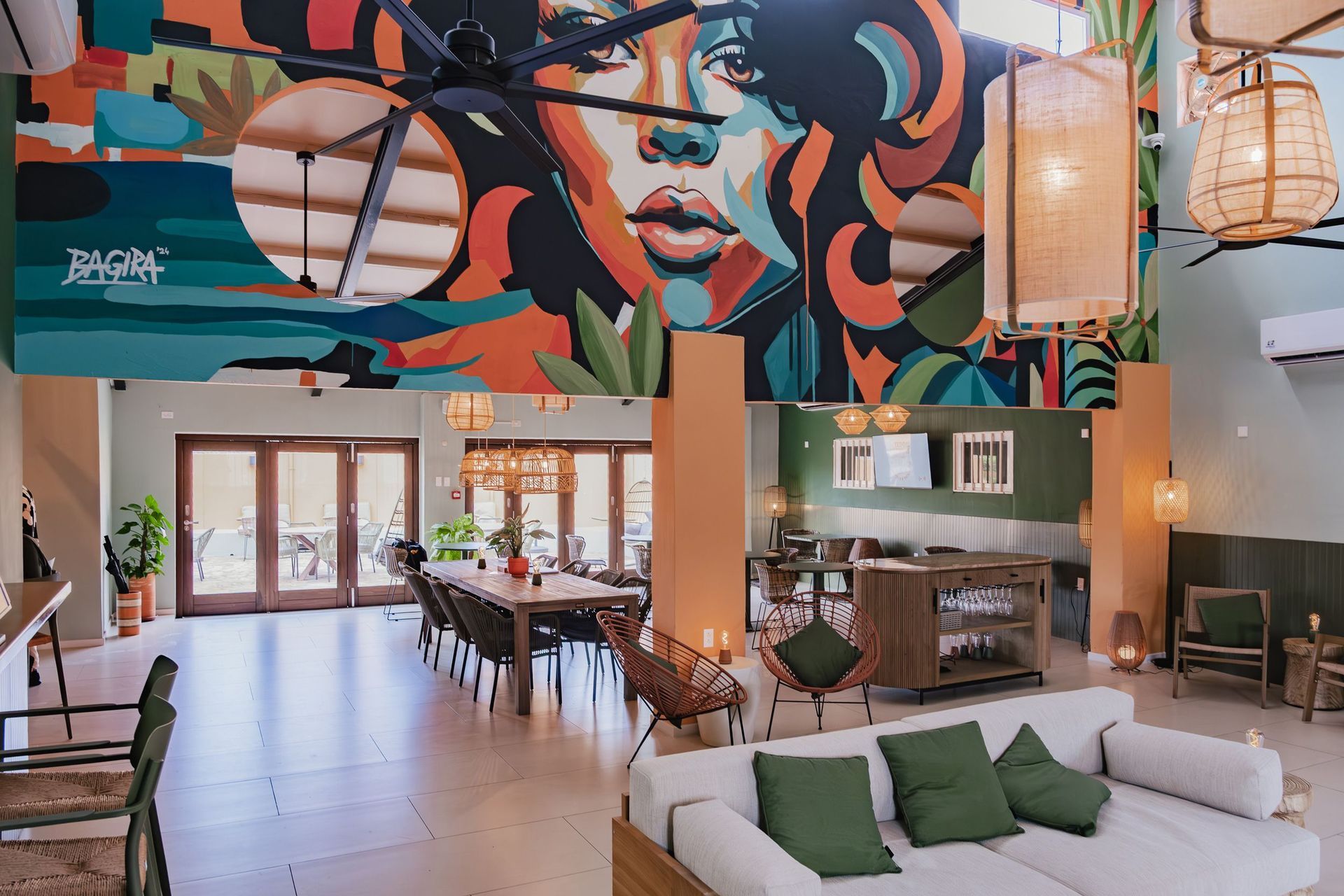 Colorful mural above a bright lounge with sofas, tables, and hanging lanterns in an open cafe space