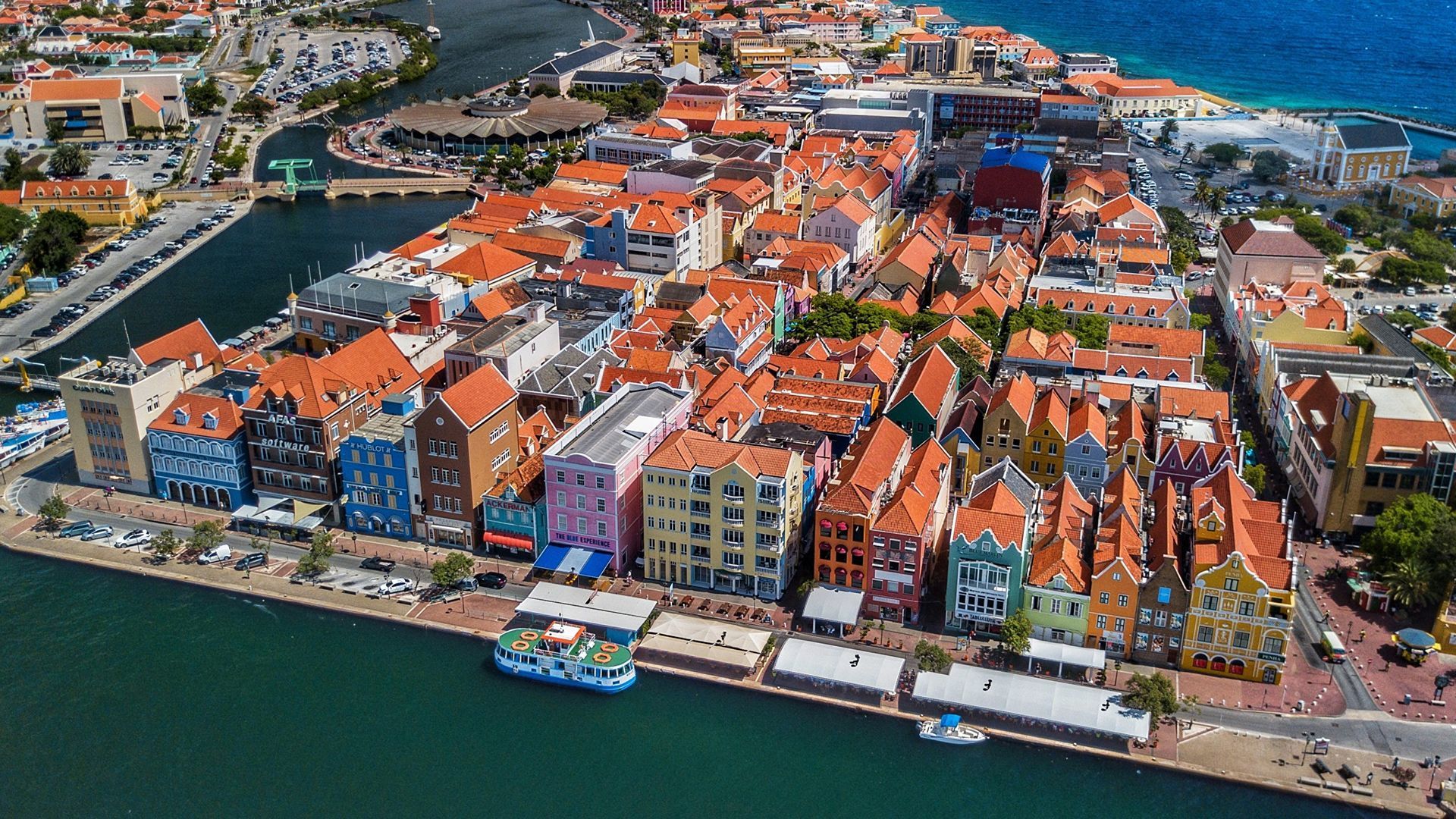 Aerial view of a colorful waterfront town with red-roofed buildings and boats along the harbor.