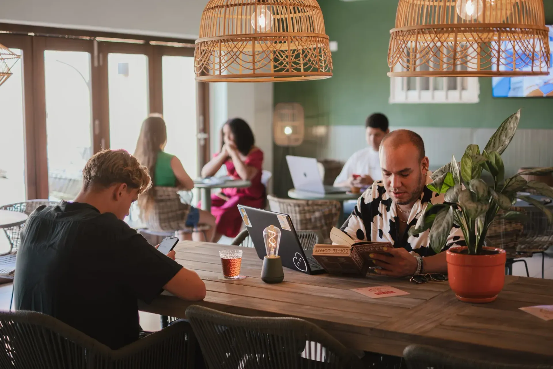 Stylish café lounge with green walls, hanging lights, colorful mural, and people seated at tables