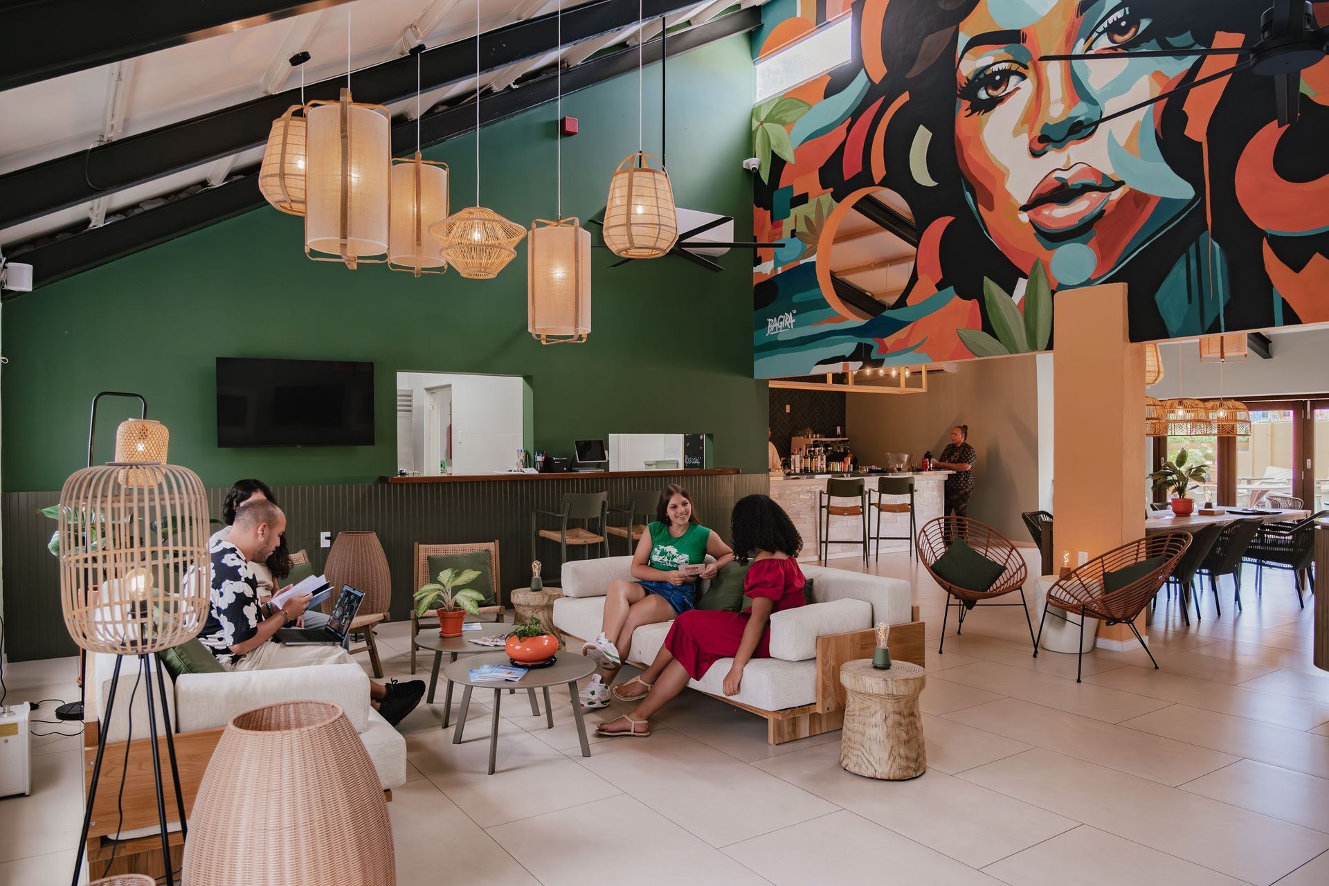 Stylish café lounge with green walls, hanging lights, colorful mural, and people seated at tables