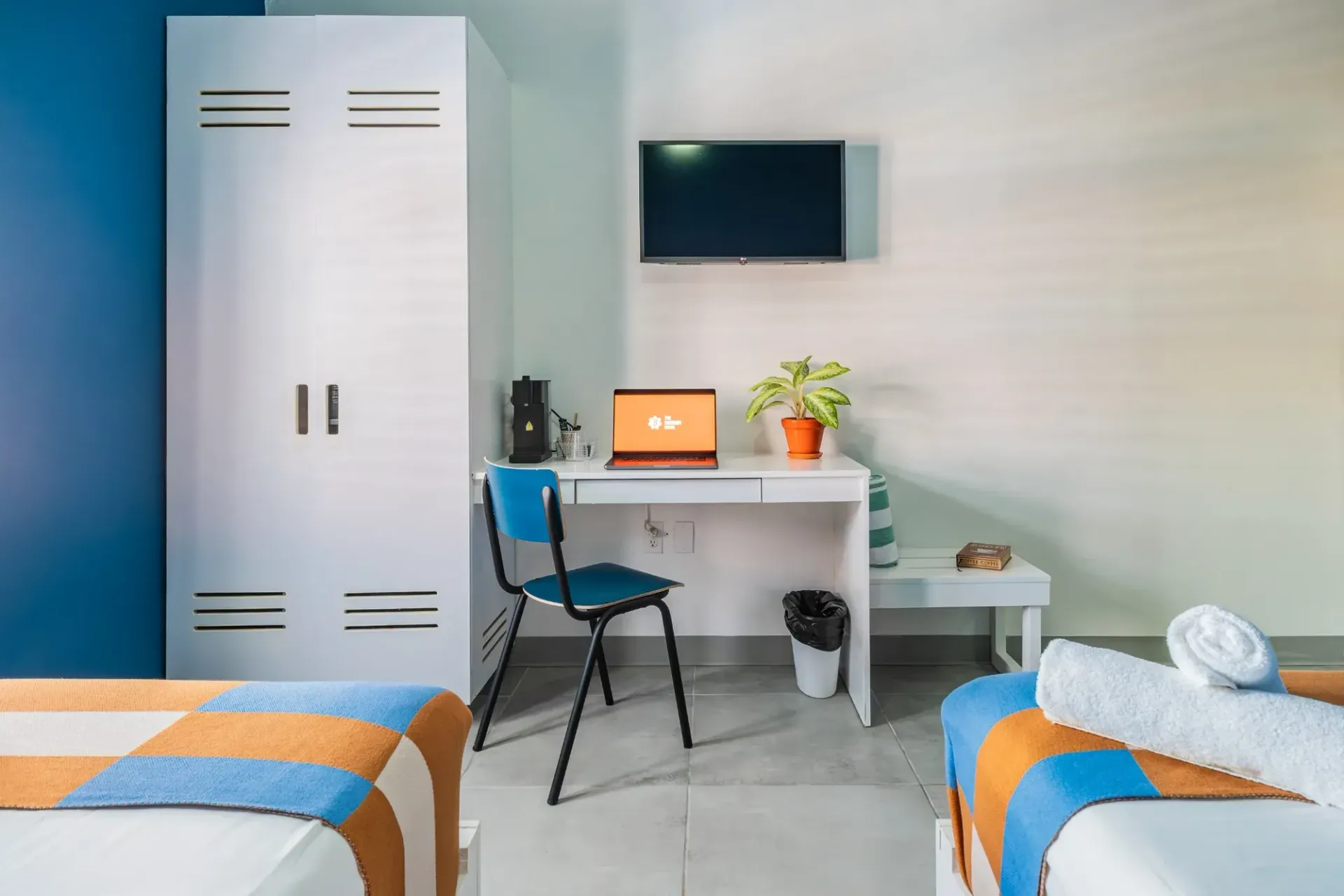 Modern bedroom desk by a window with a red laptop, chair, plants, and colorful decor