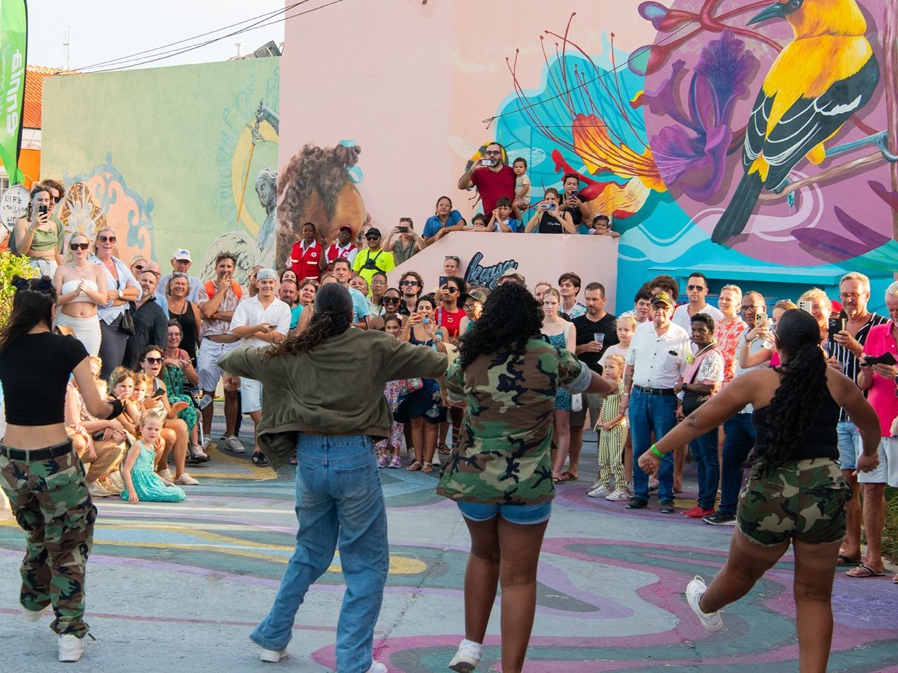 Crowd watches performers dancing in a colorful outdoor mural courtyard