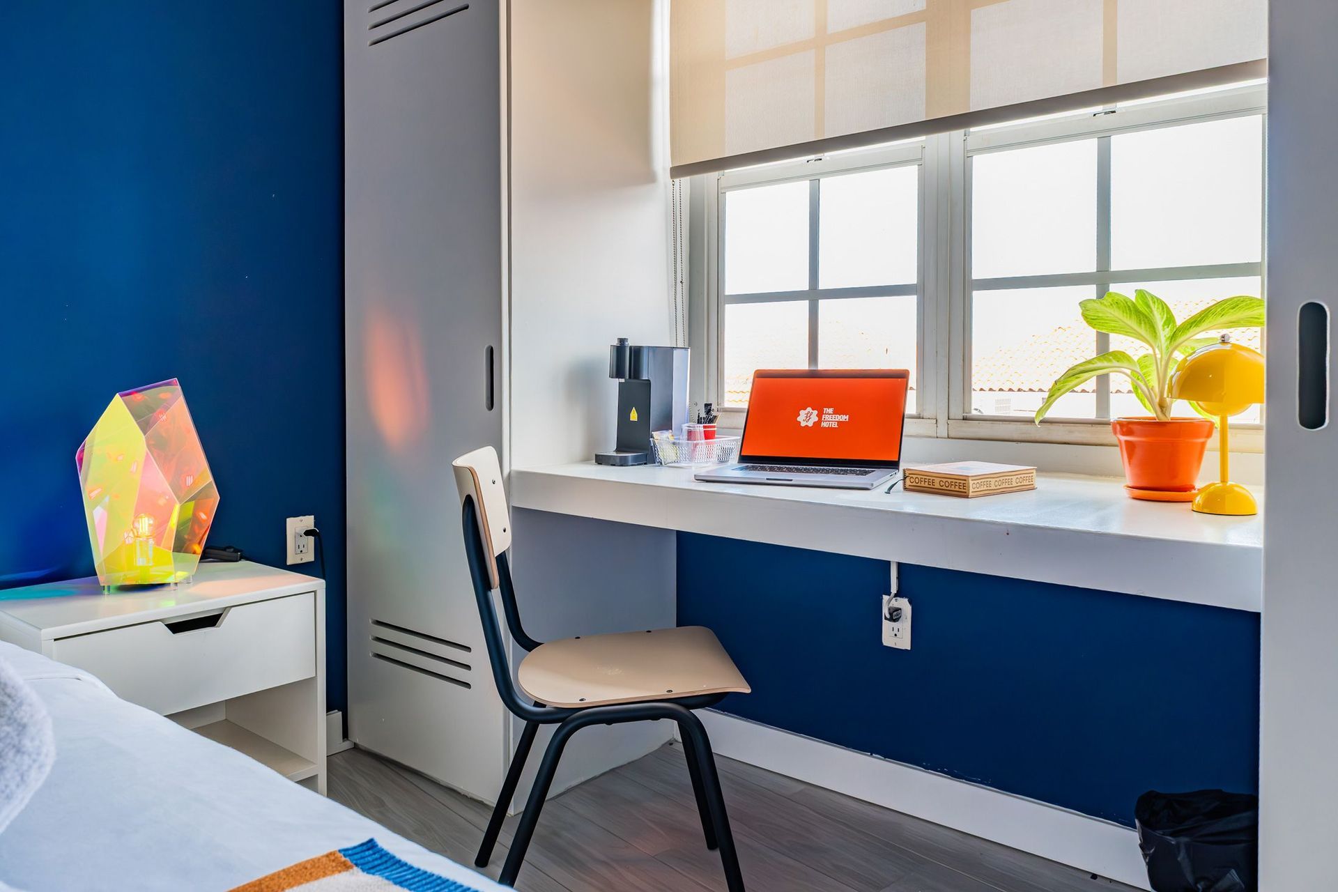 Modern bedroom desk by a window with a red laptop, chair, plants, and colorful decor