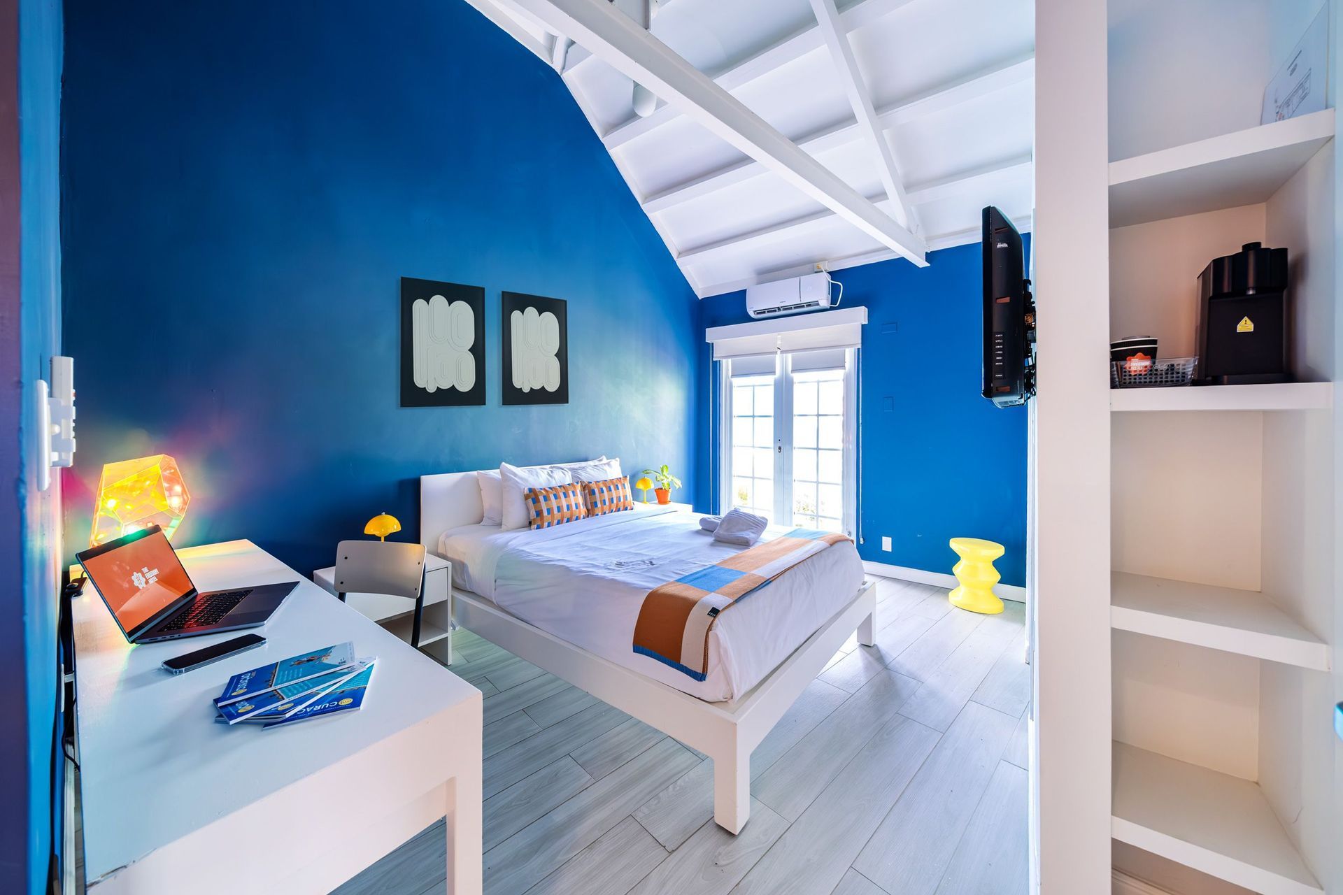 Bright blue bedroom with white bed, desk, shelves, and high vaulted ceiling
