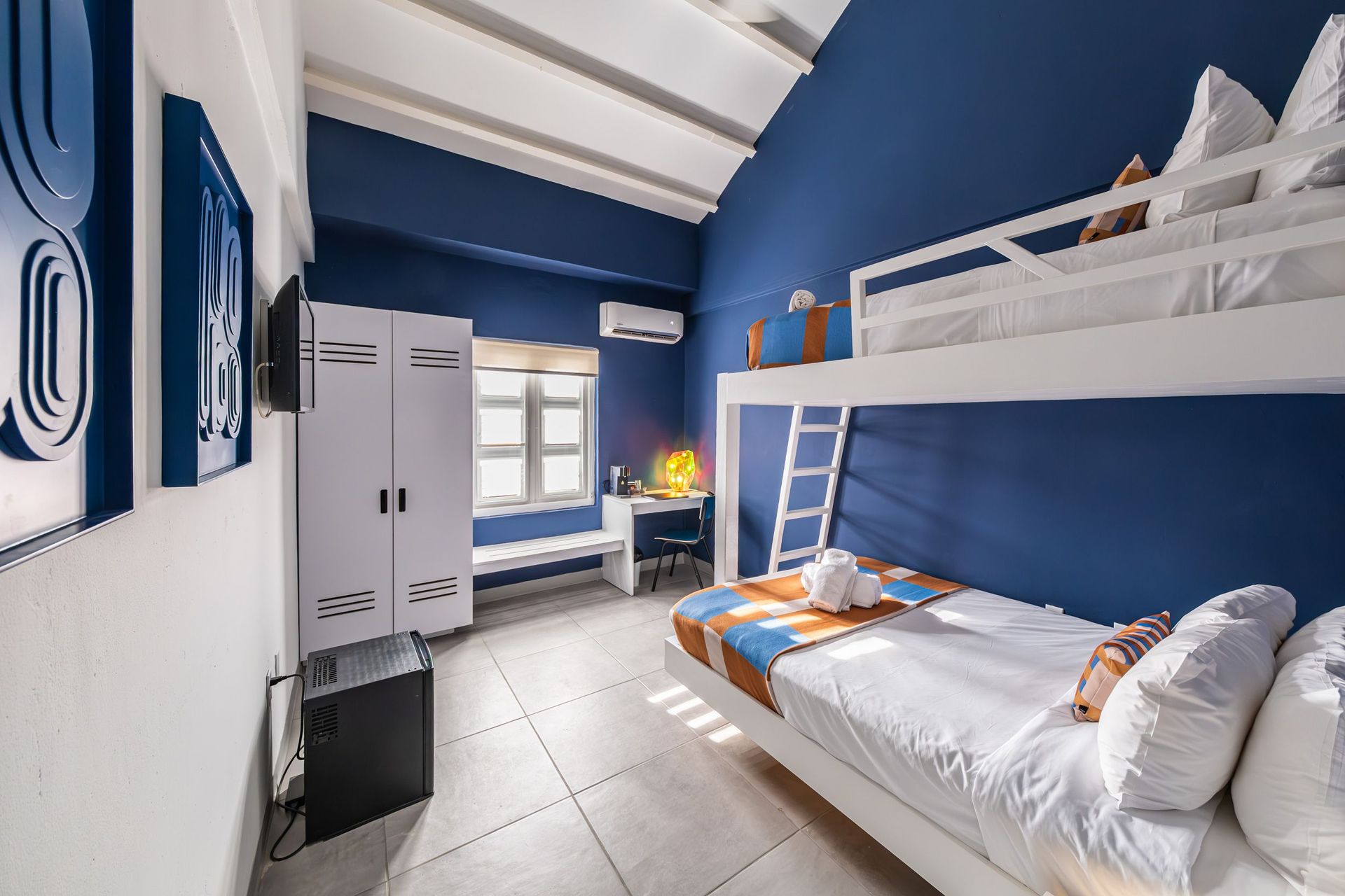 Compact bedroom with blue walls, bunk beds, a white wardrobe, and a window letting in daylight