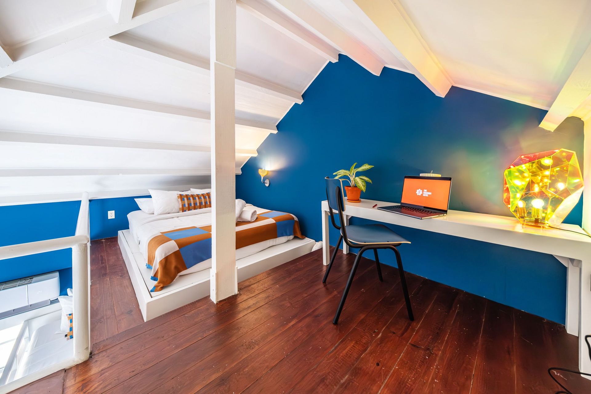 Loft bedroom with blue accent wall, desk, chair, bed, and skylight.
