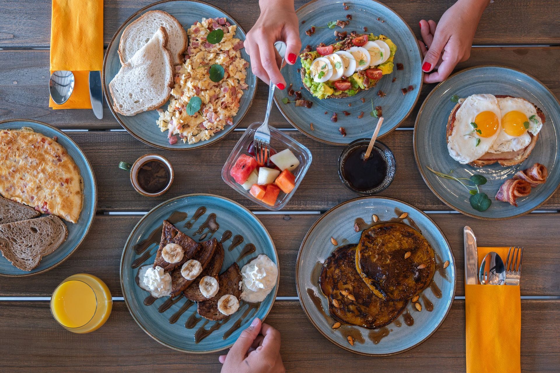 Overhead view of a shared breakfast table with pancakes, eggs, fruit, coffee, and orange juice