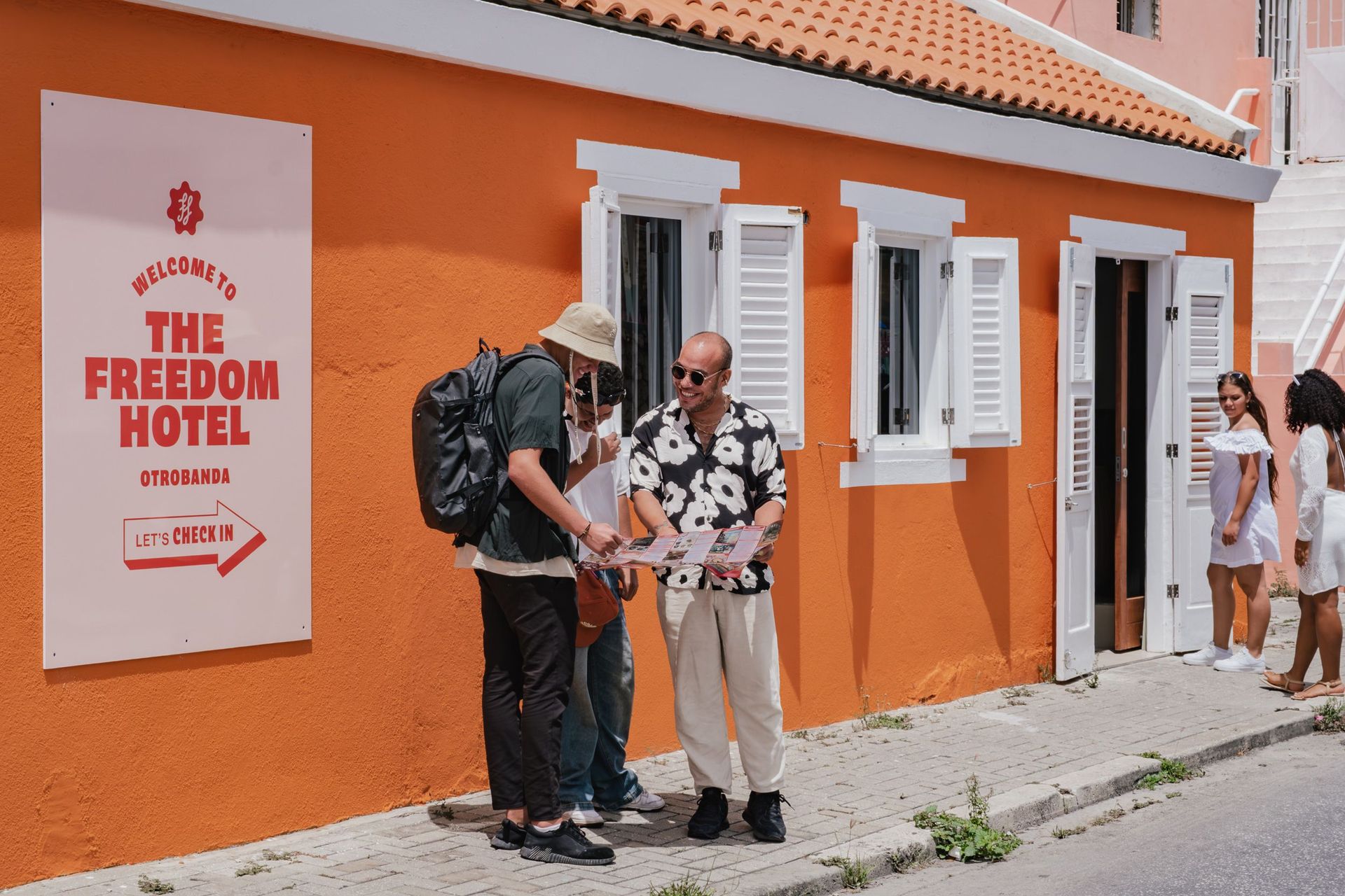 People outside The Freedom Hotel, with orange facade and white shutters, talking near the entrance.