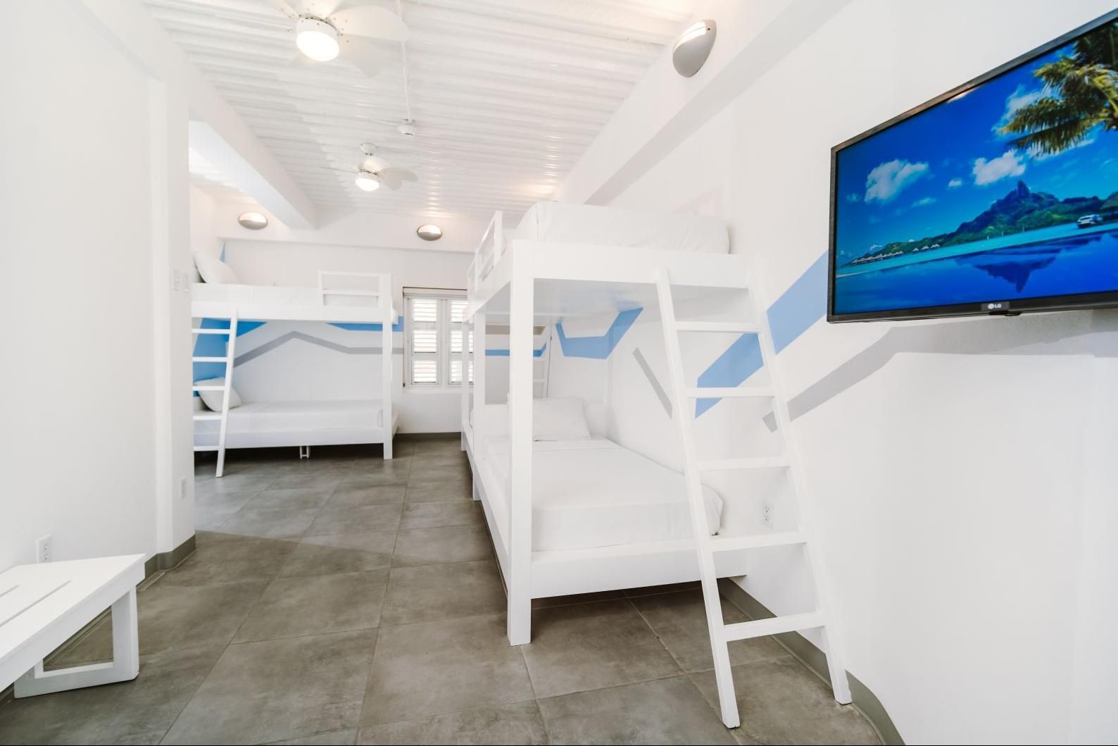 Bright white bunk-bed dorm room with blue accents, gray floor, and wall-mounted TV