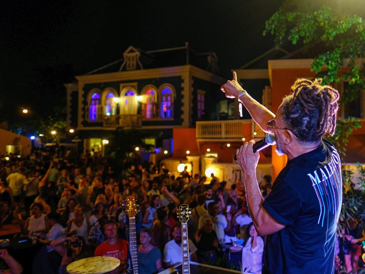 Singer performing to a large crowd at night, with colorful lights on the building behind him