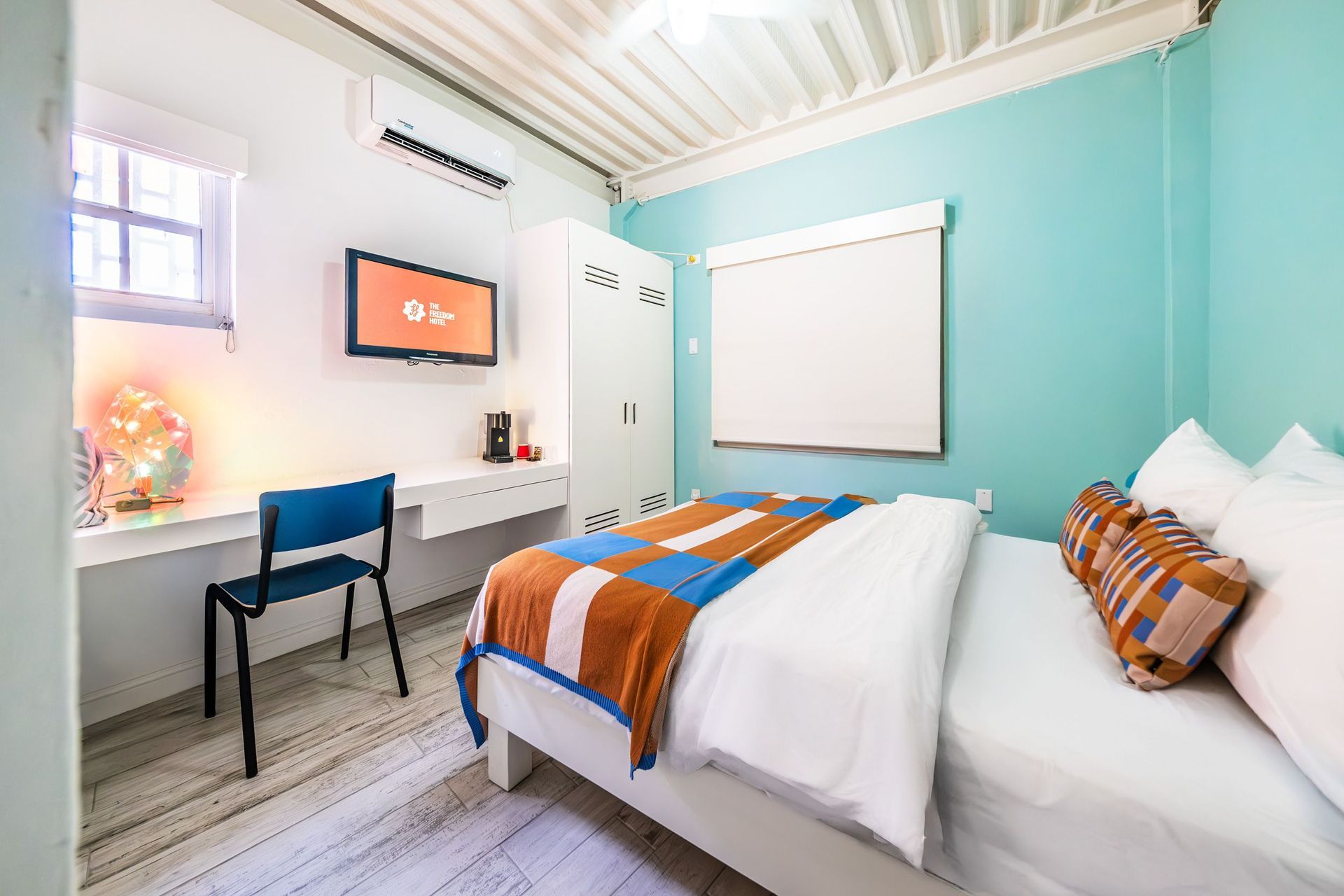 Bright bedroom with twin beds, teal walls, desk, and a window with a white blind