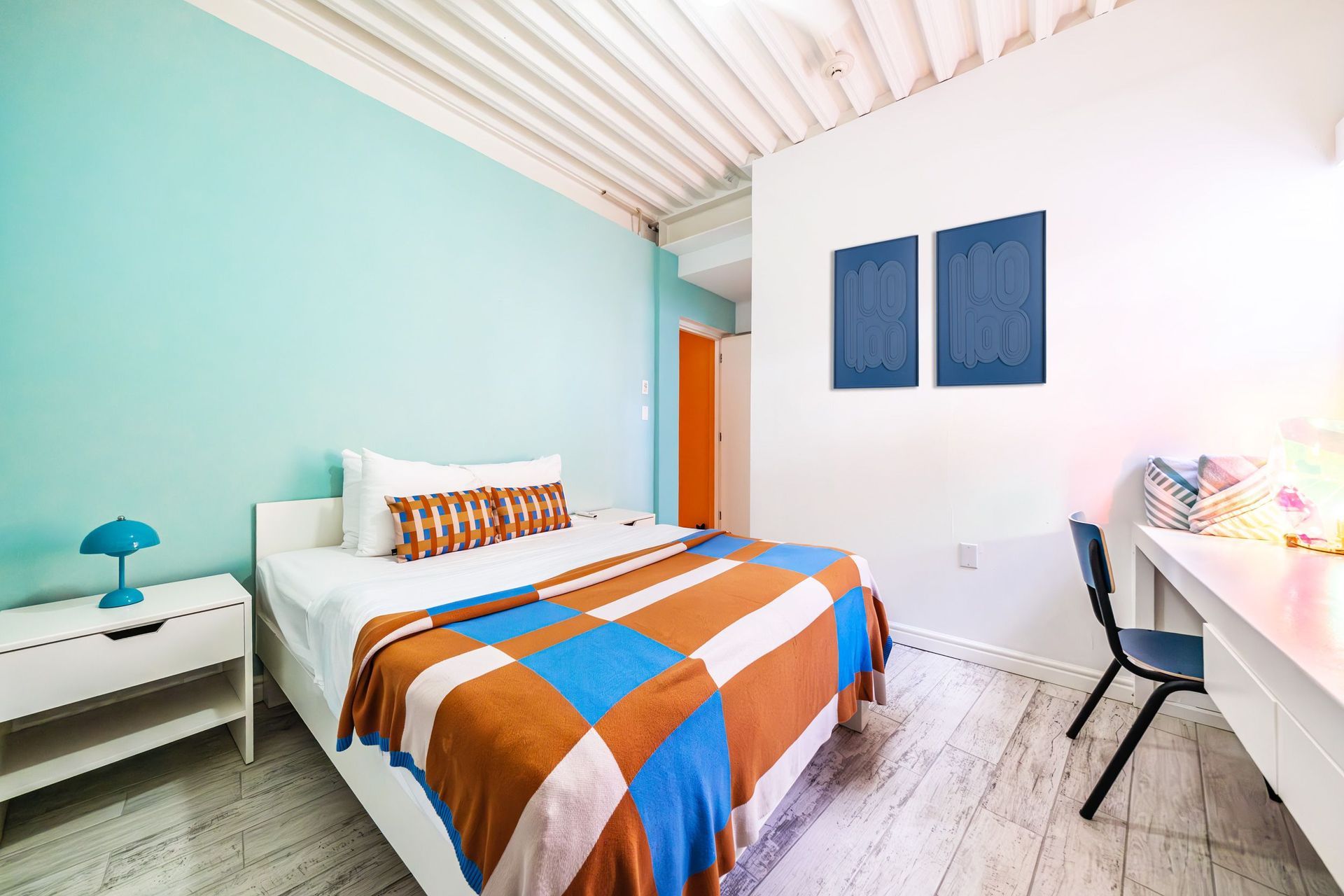 Bright bedroom with striped bedspread, white desk, blue accents, and mint green wall