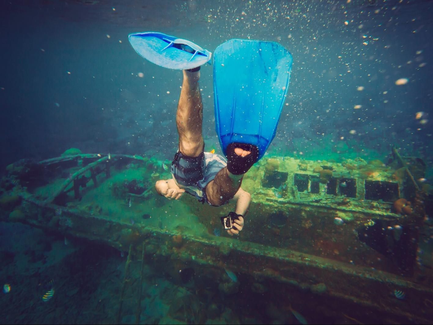 Scuba diver exploring a sunken ship, with blue fins and snorkel in murky underwater water.