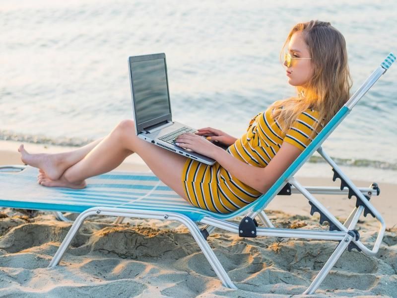 Person using a laptop while reclining on a beach chair by the water