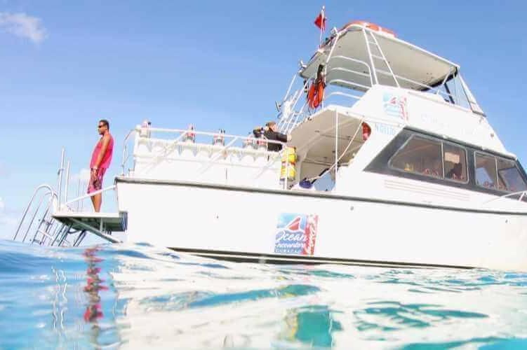 White yacht on clear blue water with two people standing on the deck under a bright sky