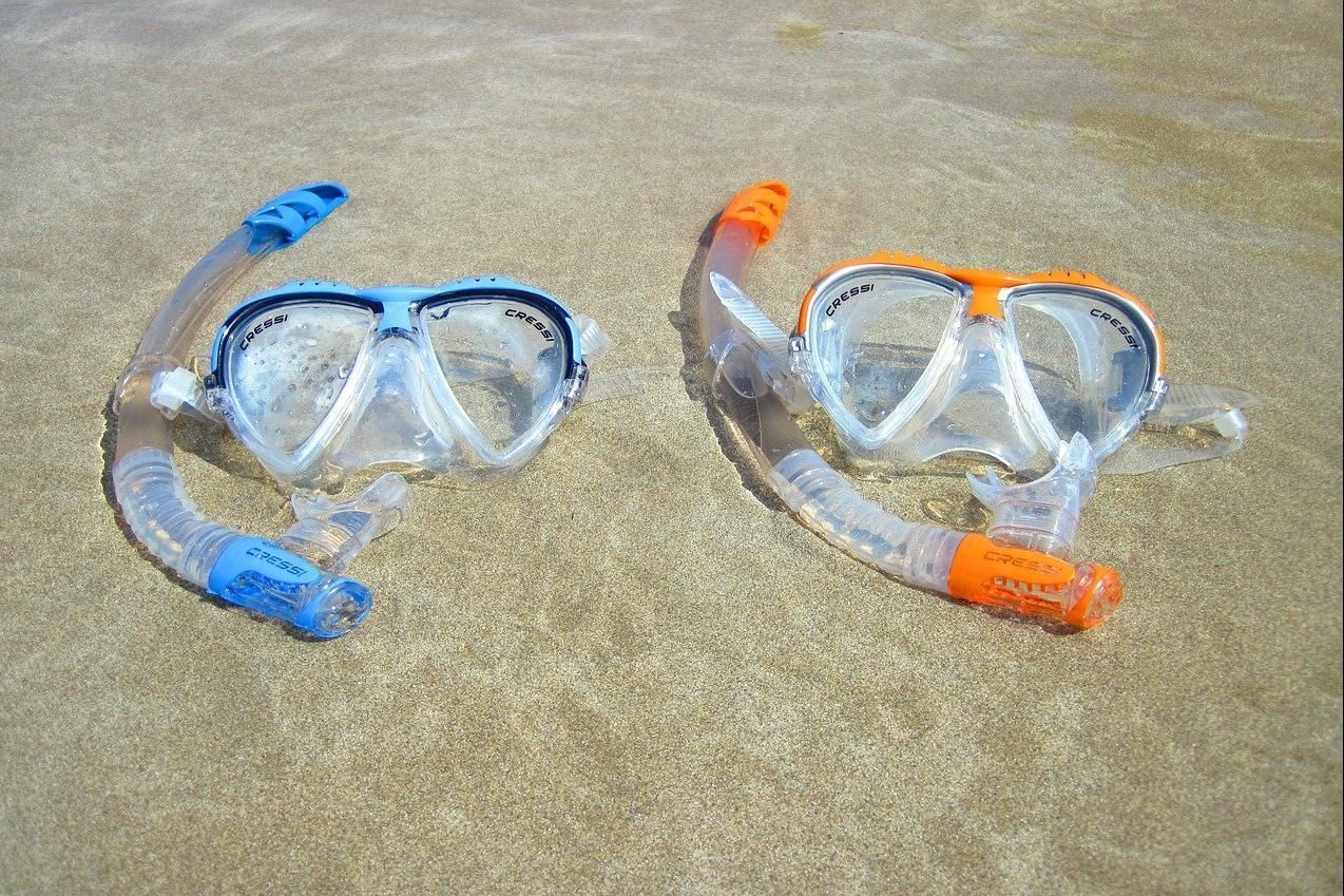 Two snorkeling masks with blue and orange snorkels lying on sand