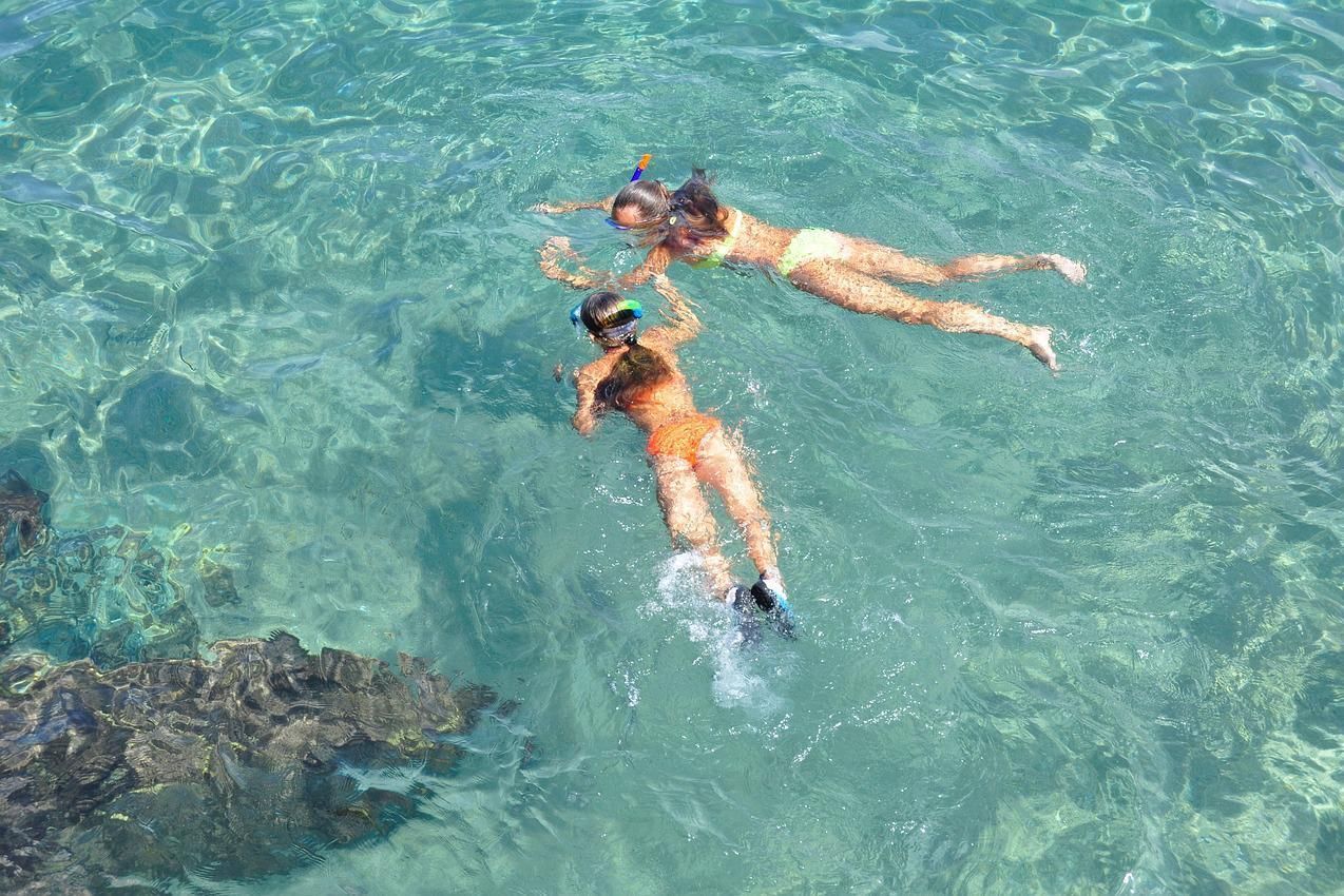 Two snorkelers floating in clear turquoise water near a rocky reef