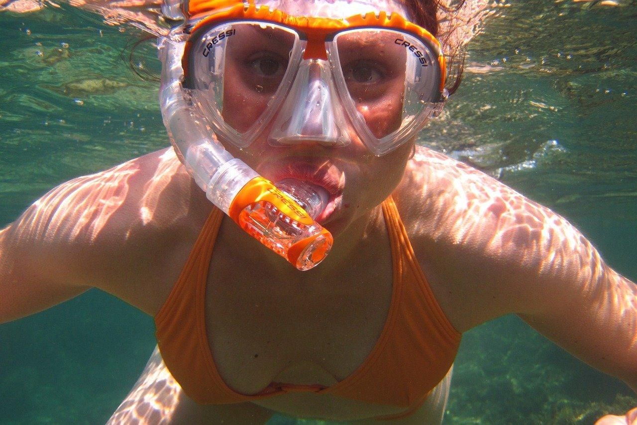 Snorkeler underwater in orange gear, wearing a mask and snorkel, swimming toward the camera.