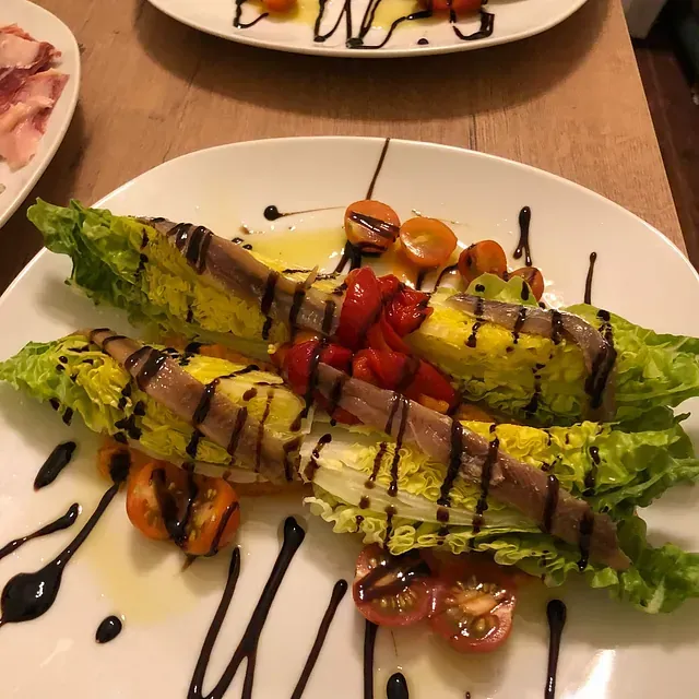 Un plato blanco cubierto con lechuga, tomates y anchoas.