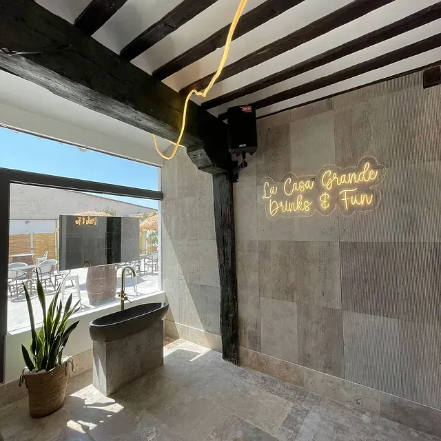 Una habitación con un letrero de neón que dice La Casa Grande bebidas y diversión.