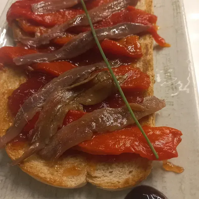Un sándwich con anchoas y pimientos en un plato