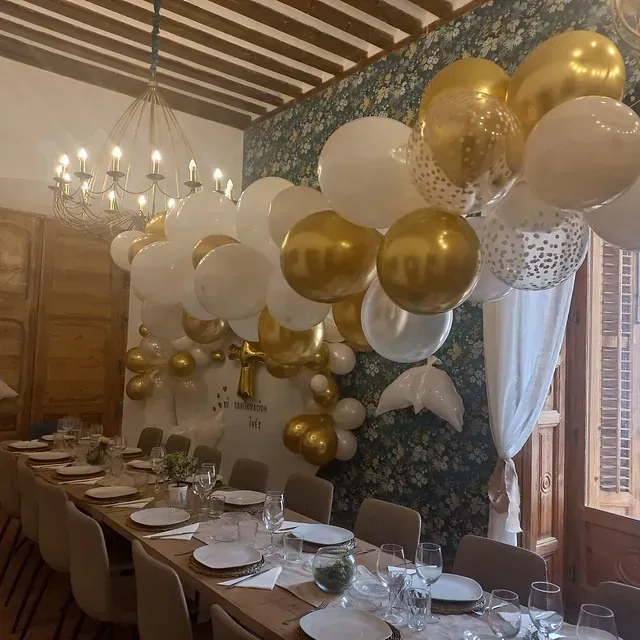 Una mesa larga con platos y vasos y globos colgando del techo.