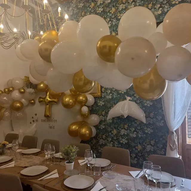 Una mesa de comedor con platos y vasos y globos colgando del techo.