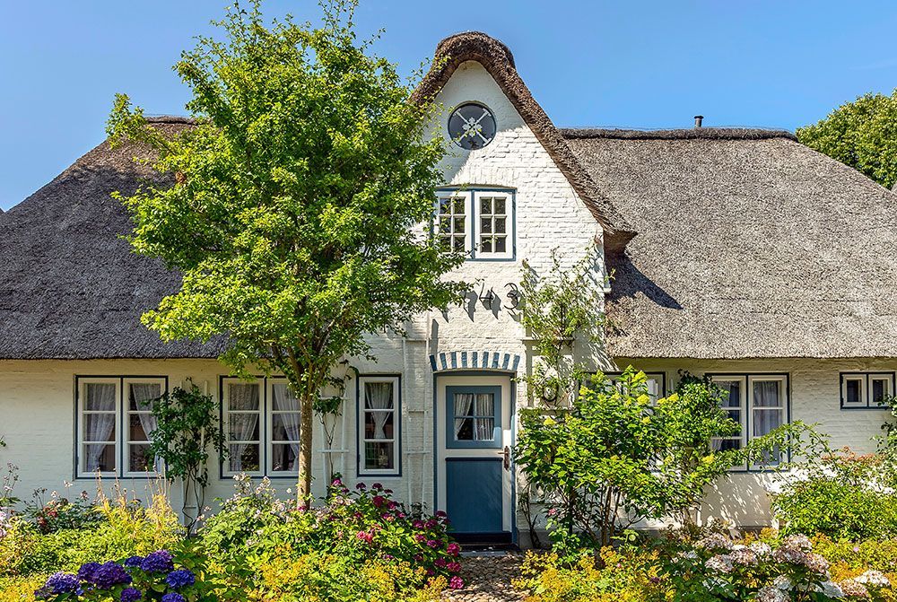 Ein weißes Haus mit Strohdach und blauer Tür