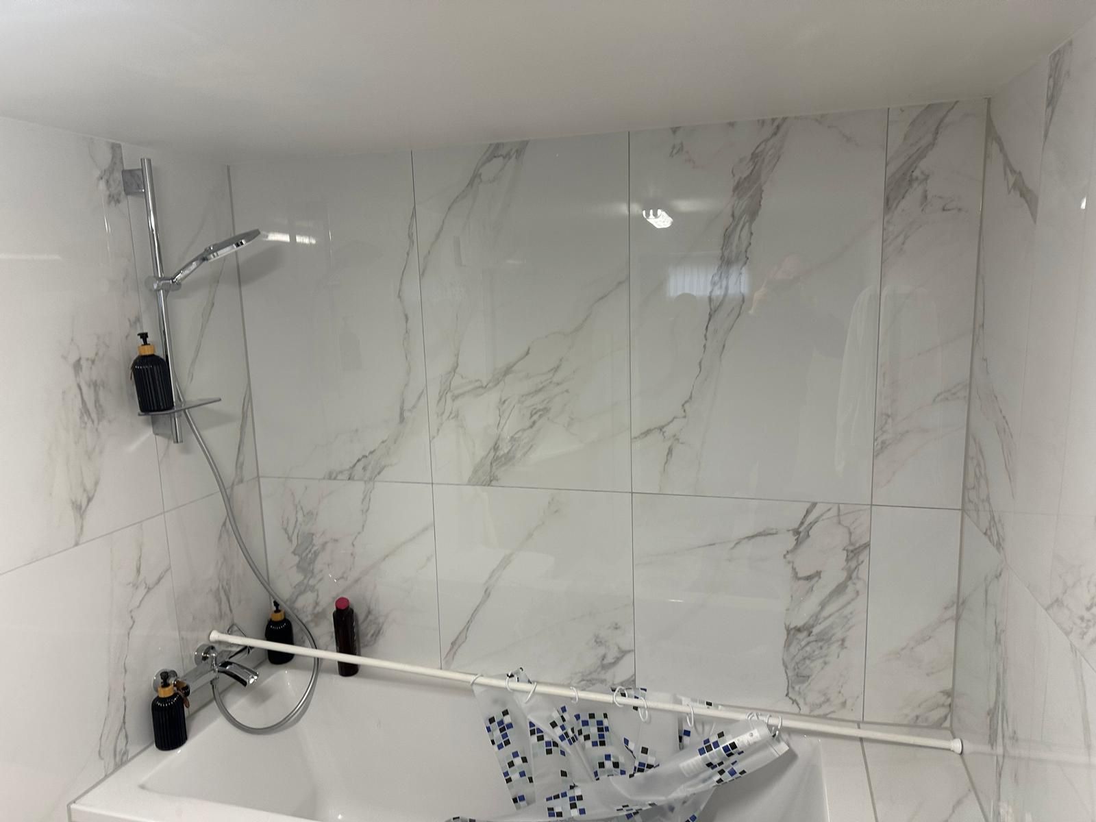 Dusche mit weißen Marmorfliesen, silbernem Duschkopf, Seifenflaschen und einem Duschvorhang über der Badewanne.