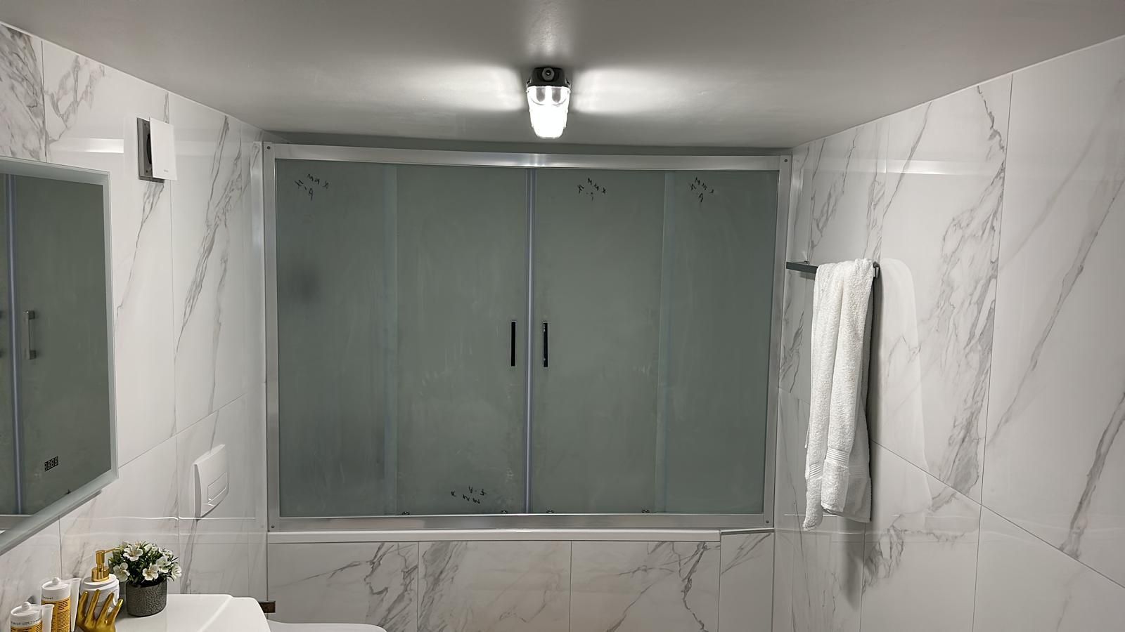 Badezimmer mit Marmorwänden, Milchglas-Duschtüren und einem Handtuch, das an einer Stange hängt.