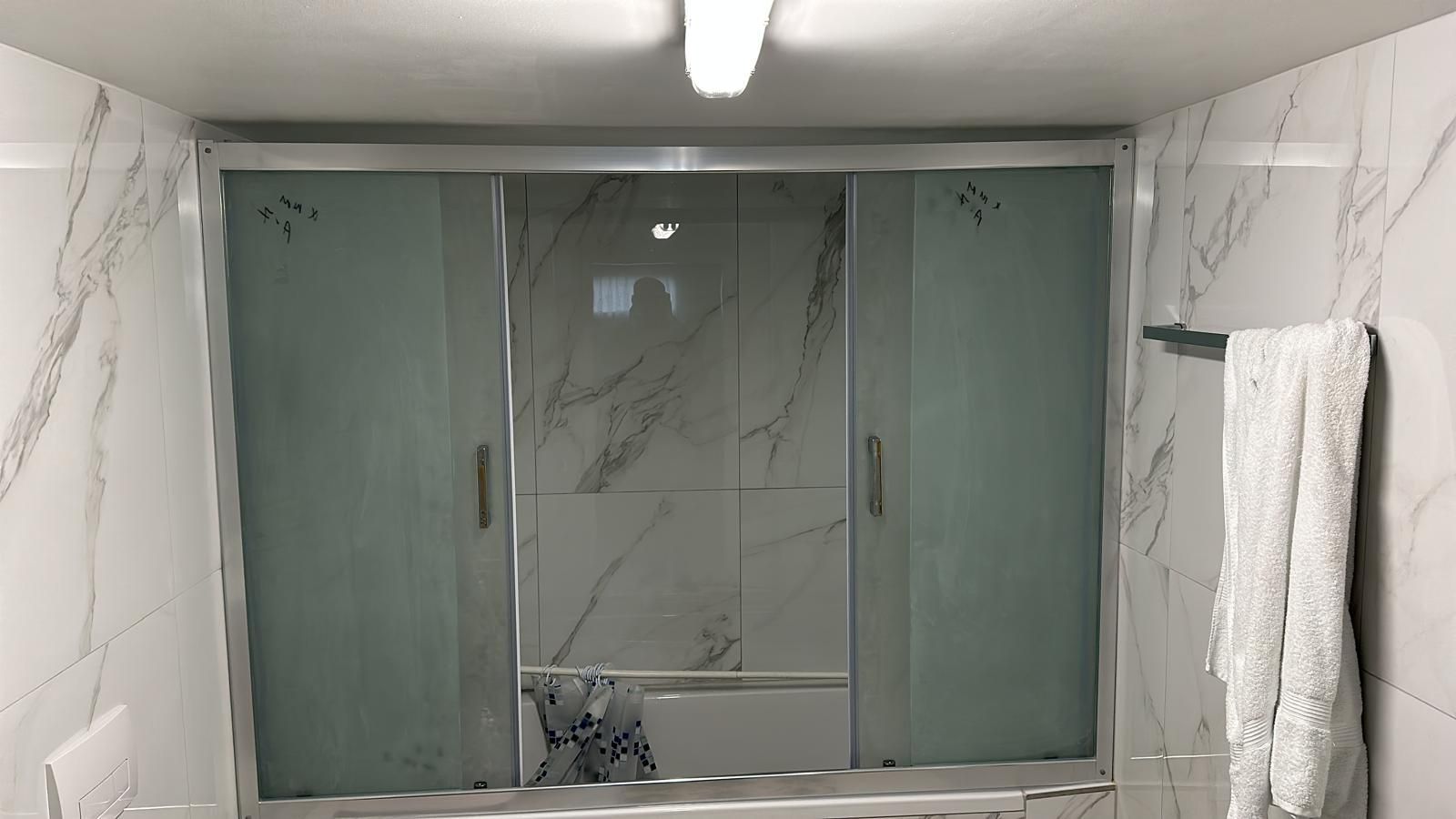 Ein Badezimmer mit einer Glasschiebetür zur Dusche und einer Wand aus Marmorfliesen. Rechts hängt ein Handtuch.