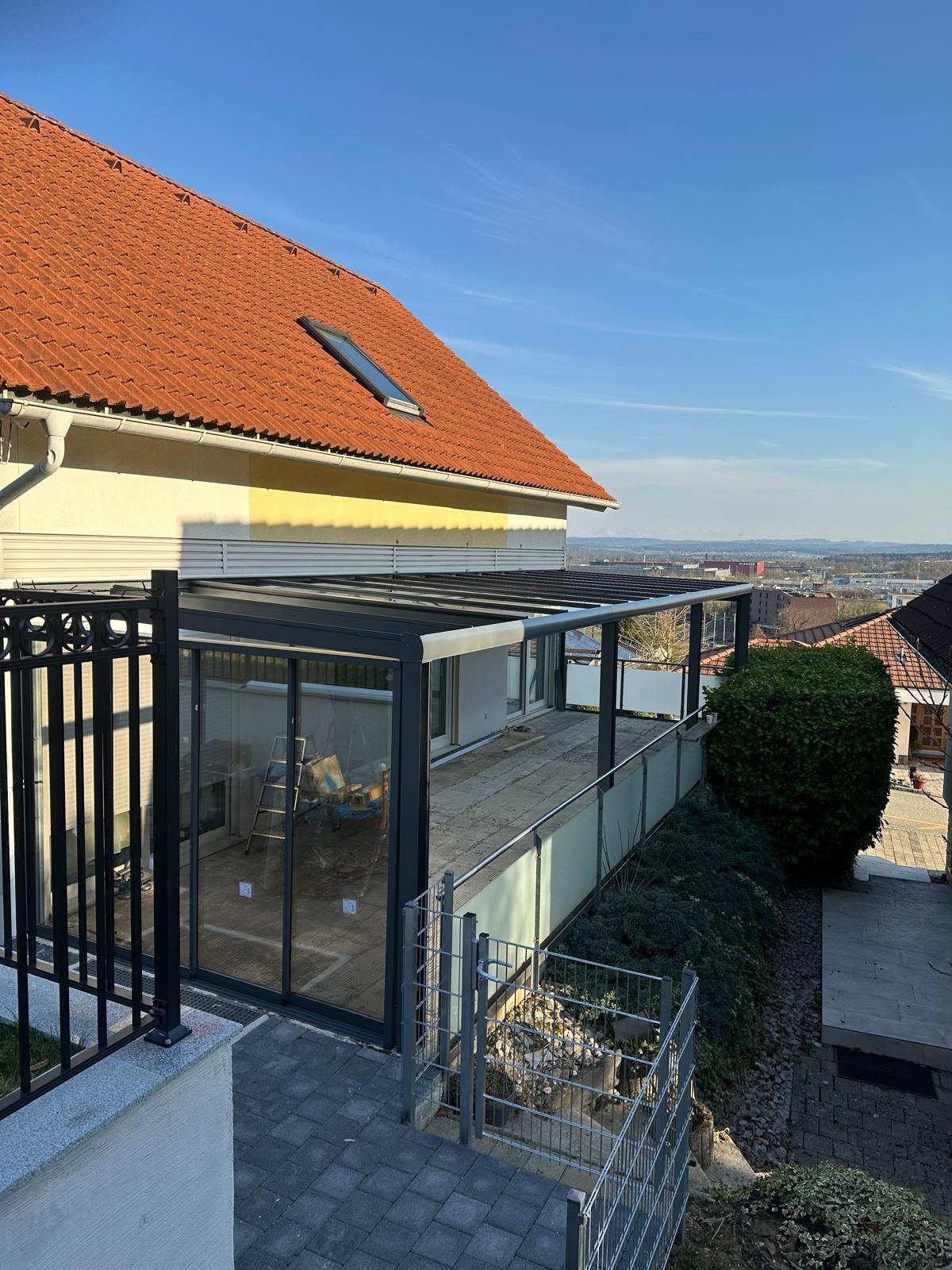 Ein Wintergarten mit Glaswänden und Flachdach, angebaut an ein Haus mit rotem Ziegeldach.
