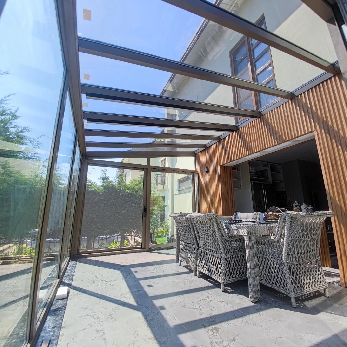 Wintergarten mit Glaswänden und Glasdach, in dem sich ein Esstisch und Stühle befinden.