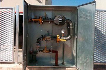 Armario metálico abierto para servicios públicos con tuberías de gas, válvulas y manómetros en su interior.