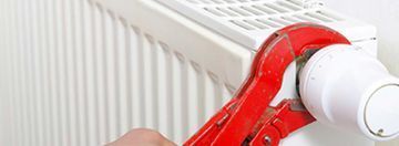 Primer plano de una válvula roja de un radiador blanco siendo girada.