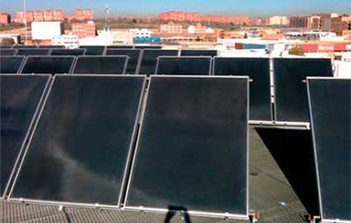 Hileras de paneles solares negros en una azotea con edificios al fondo.