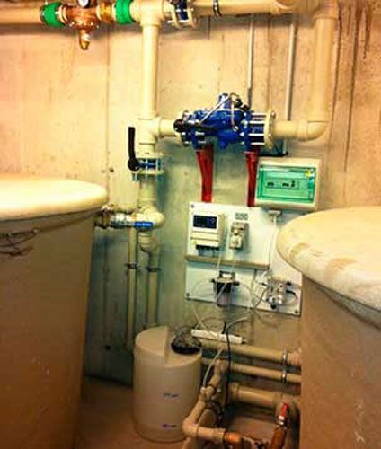 Equipos y tuberías de tratamiento de agua instalados entre dos fregaderos en un cuarto de servicio.
