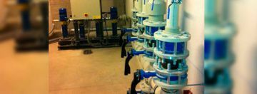 Filas de máquinas industriales azules en un pasillo de una fábrica, con equipos al fondo y un primer plano borroso.