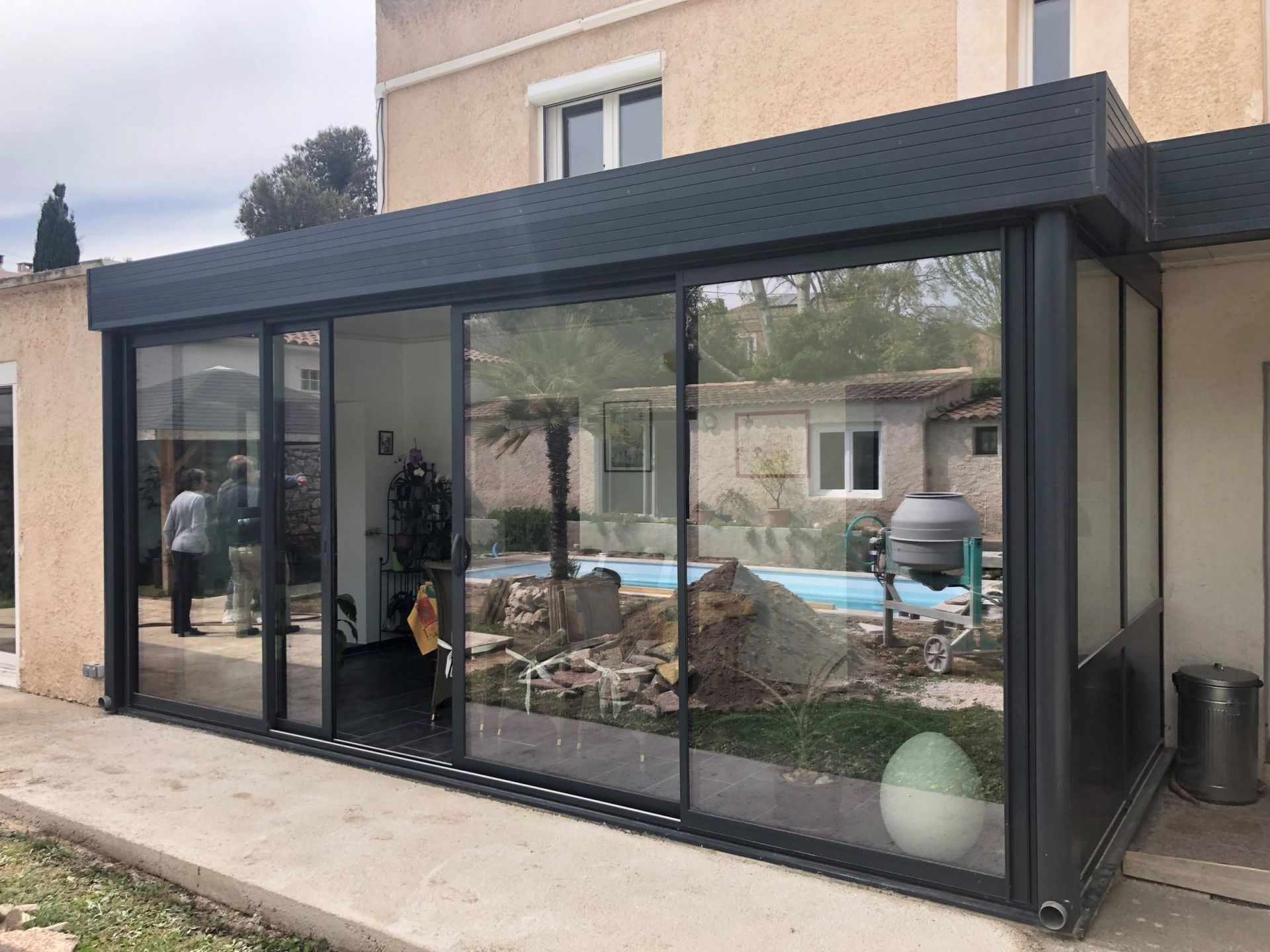 L'image présente la façade vitrée d'une maison, soulignant son architecture moderne. Les éléments environnants incluent les espaces extérieurs, les trottoirs et la structure du bâtiment.