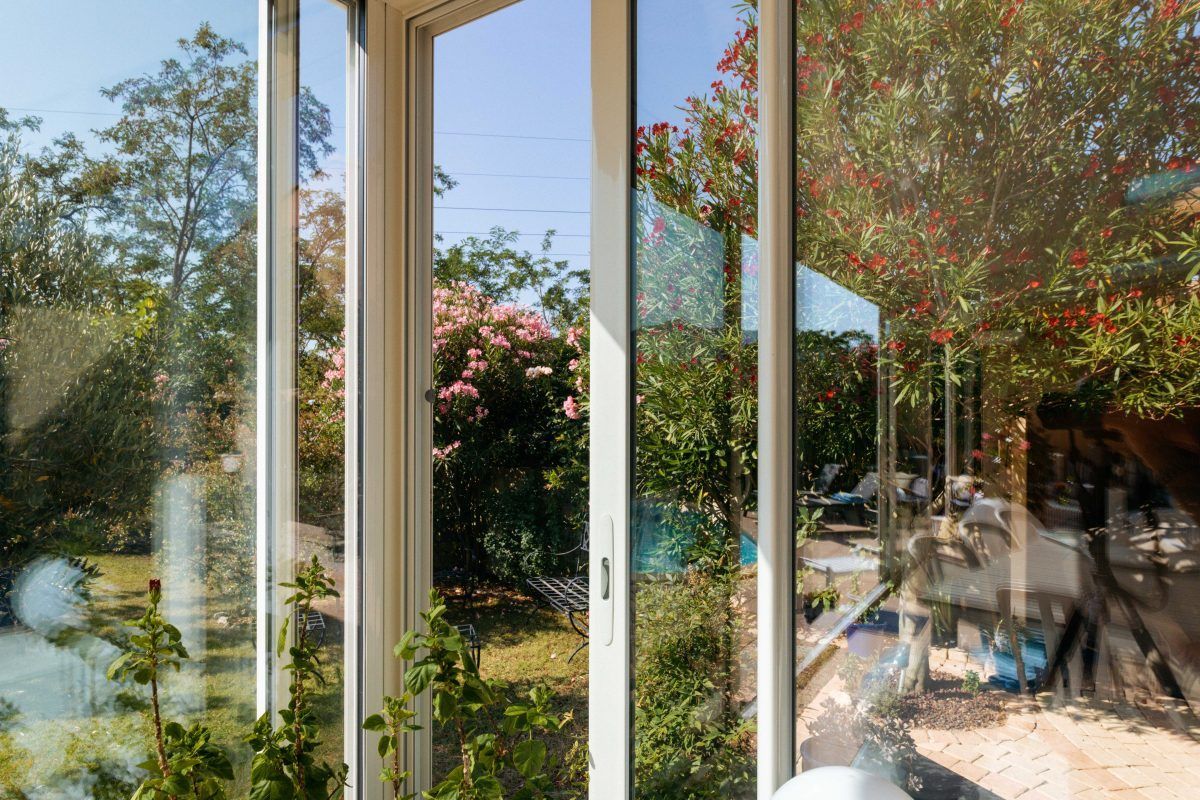 Gros plan sur les vitres d'une véranda entre-ouvertes donnant sur un jardin avec de nombreux végétaux