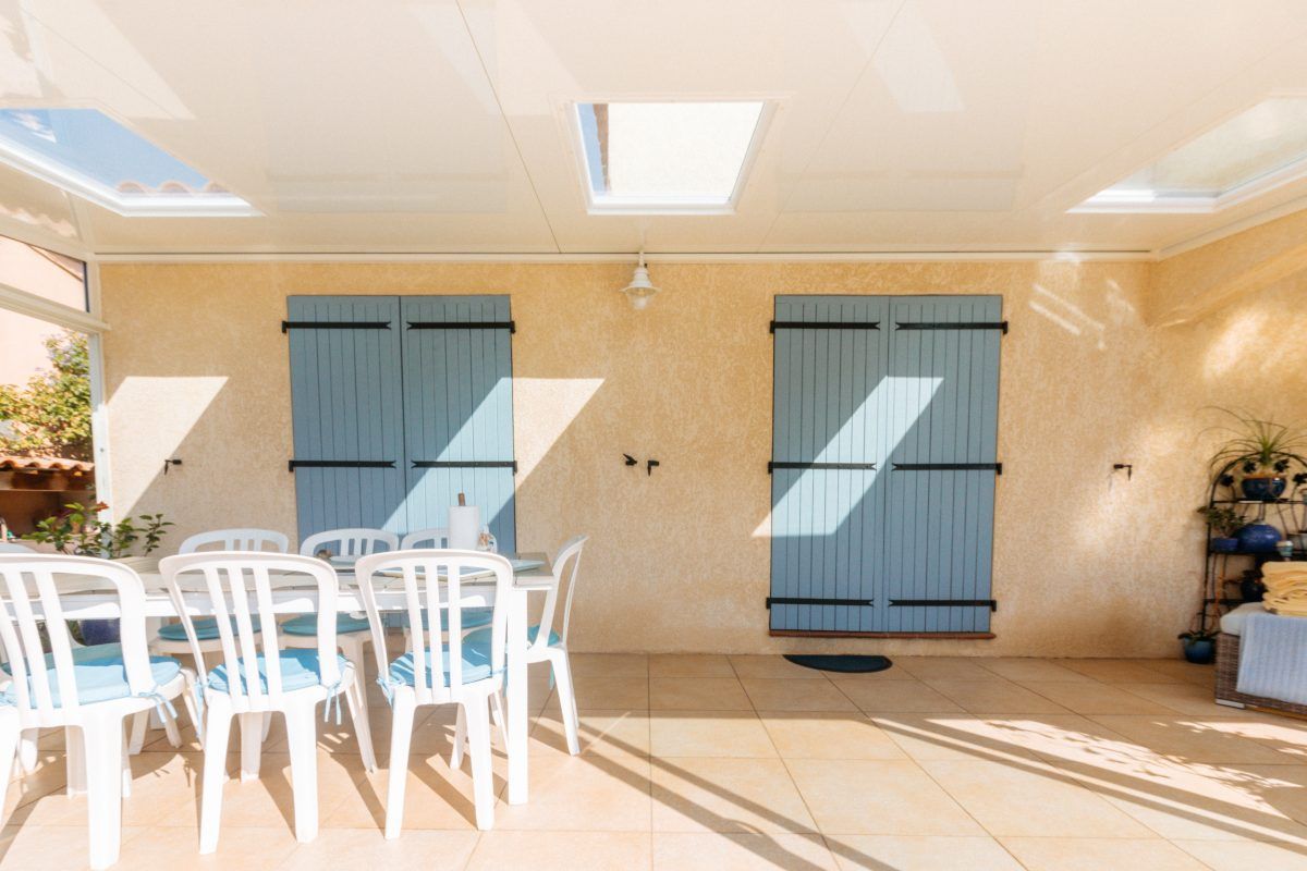 Intérieur de véranda avec deux portes fenêtres aux volets fermés ainsi qu'une table et des chaises
