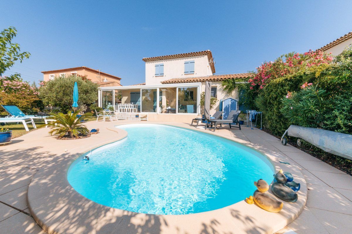Une piscine paisible située dans le jardin d'une maison avec une véranda. Entourée d'une végétation luxuriante et d'équipements de loisirs, elle crée une atmosphère extérieure relaxante.